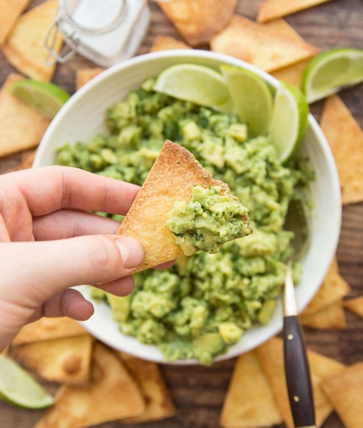 close up over shot of guac on tortilla chips with bowl of guac in the background surrounded by chips