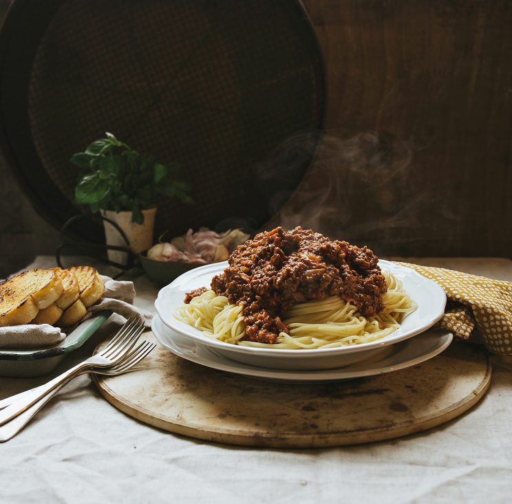 bolognese served on spaghetti with basil, garlic bread and garlic in the background