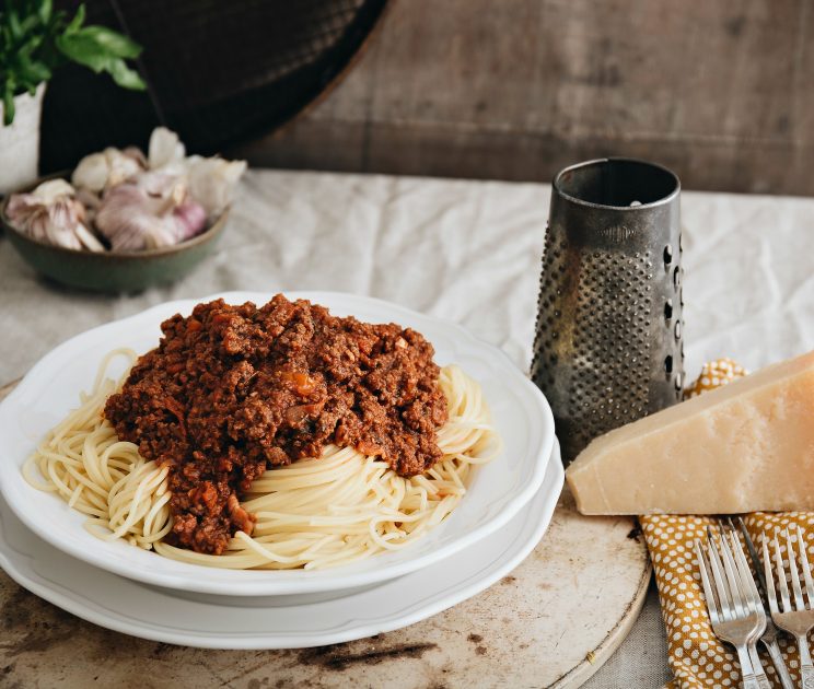 closeup shot of bolognese on spaghetti with parmesan next to it