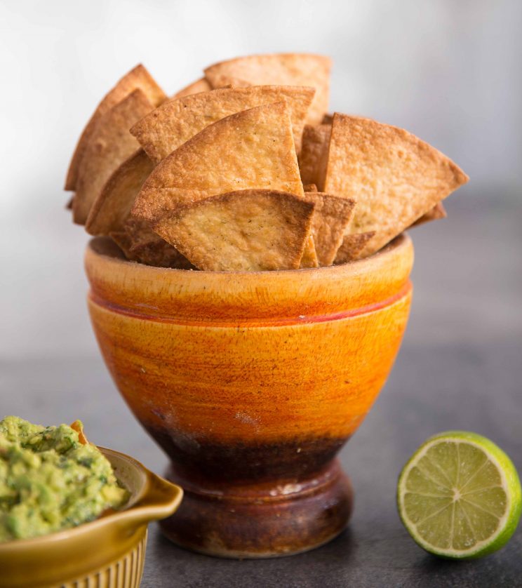 Homemade Baked Tortilla Chips in a pot with guac and lime in the background