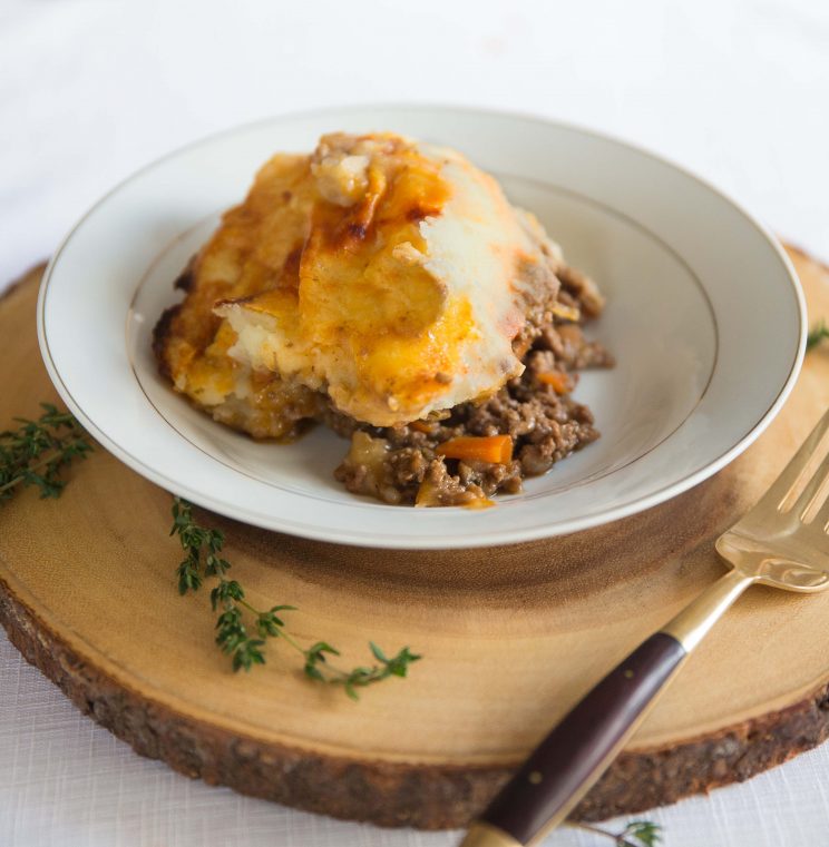 cottage pie served in white bowl on wooden board with gold fork on the side