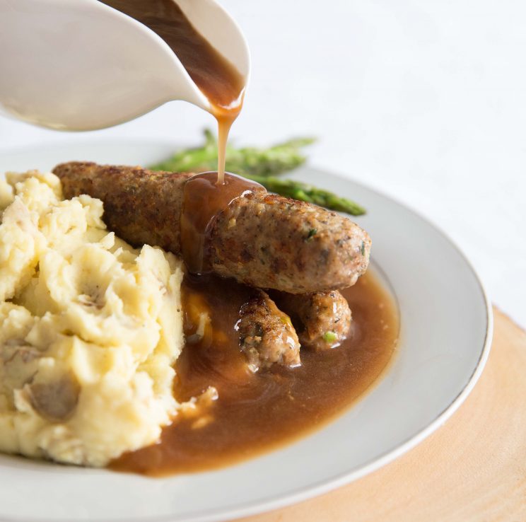 pouring gravy over sausages and mash on white plate