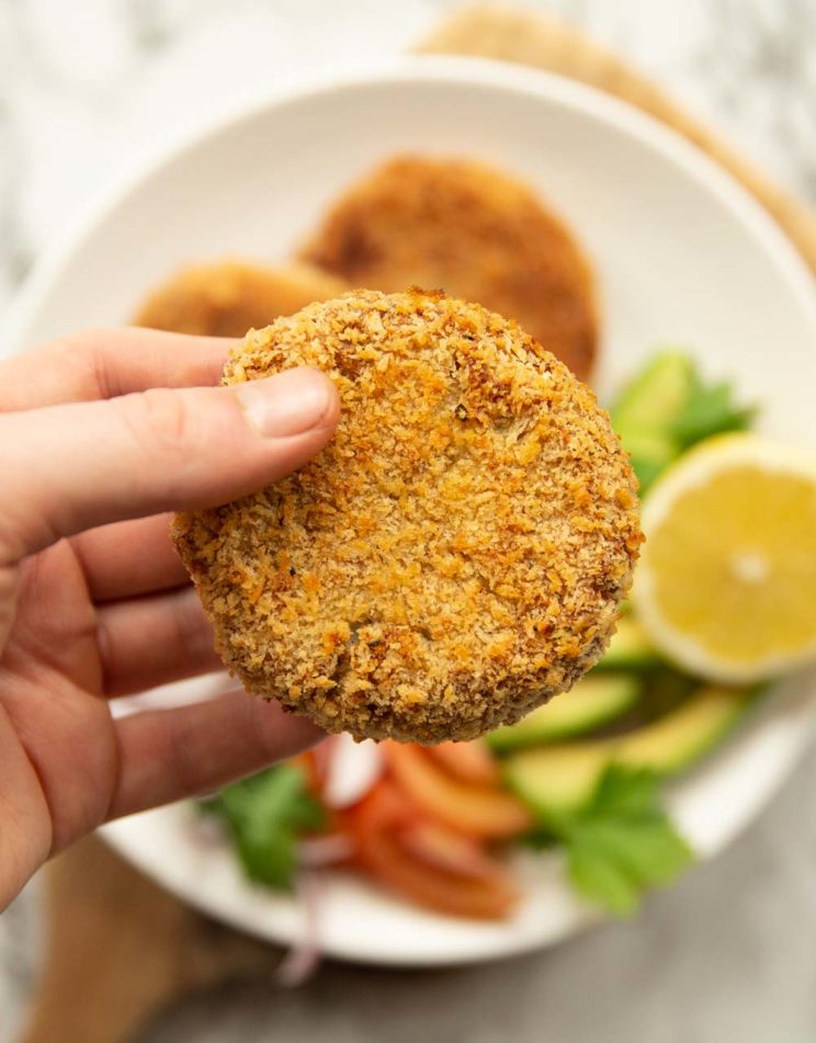 holding tuna pattie up to camera with salad blurred in the background