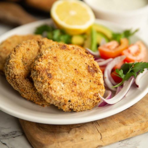 tuna patties plated with salad on white plate with dip and more patties blurred in background