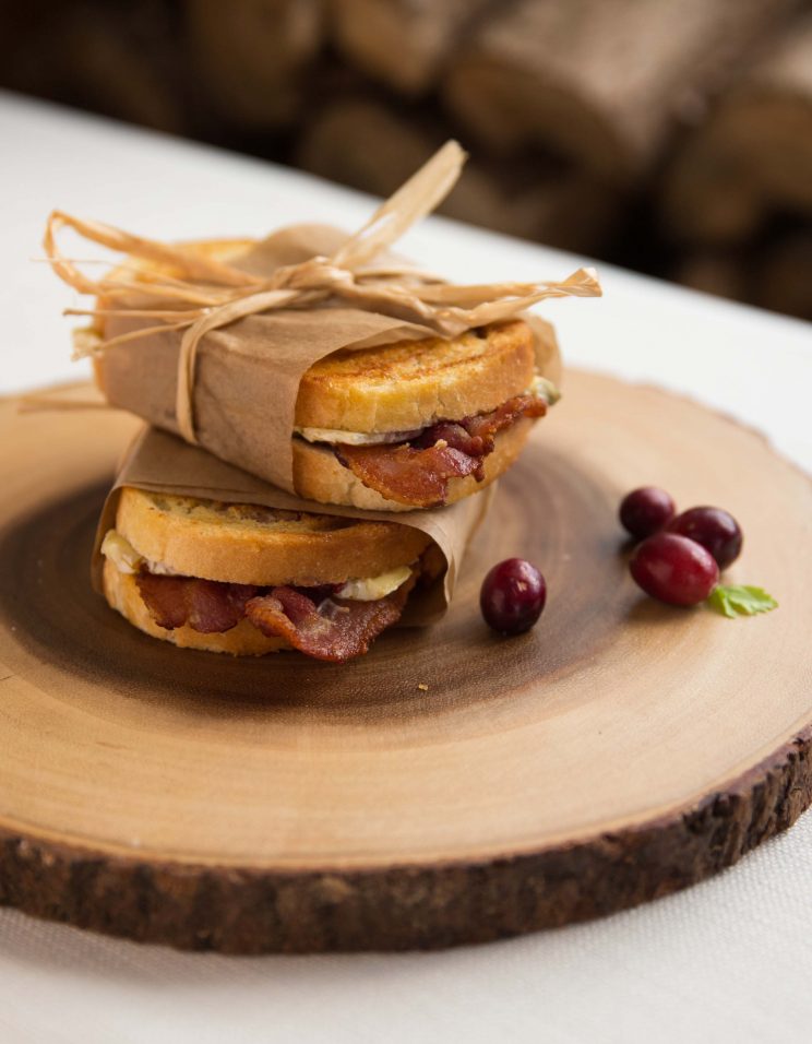 two grilled cheese stacked on each other wrapped in parchment paper on wooden board