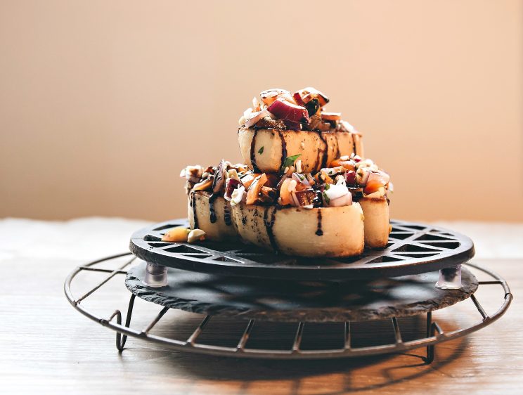 3 pieces of bruschetta stacked on each other on platform with balsamic glaze dripping down