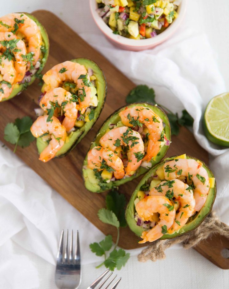 overhead shot of stuffed avocados lined up on chopping board garnished with cilantro/coriander