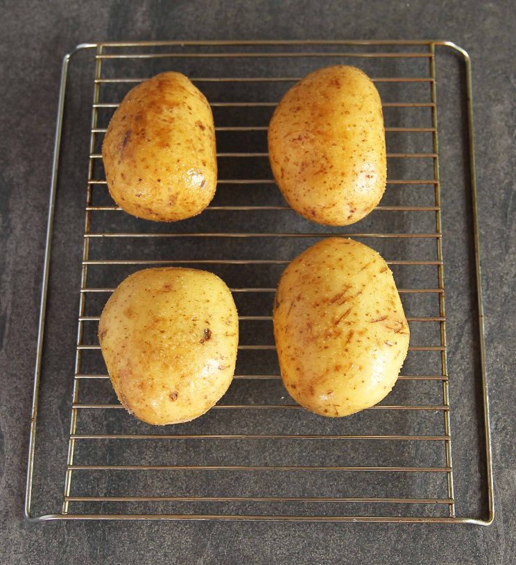 4 baked potatoes on a wire rack ready for the oven