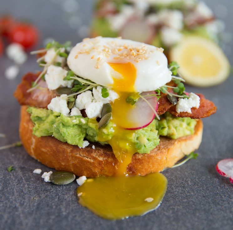 closeup shot of yolk pouring out of poached egg down smashed avocado on toast