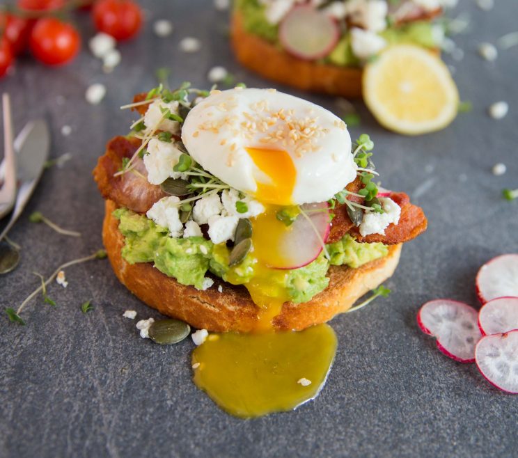 smashed avocado on toast with yolk pouring out of poached egg on top