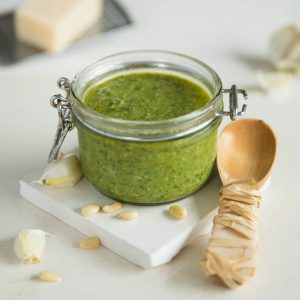 basil pesto in glass pot with serving spoon on white slate