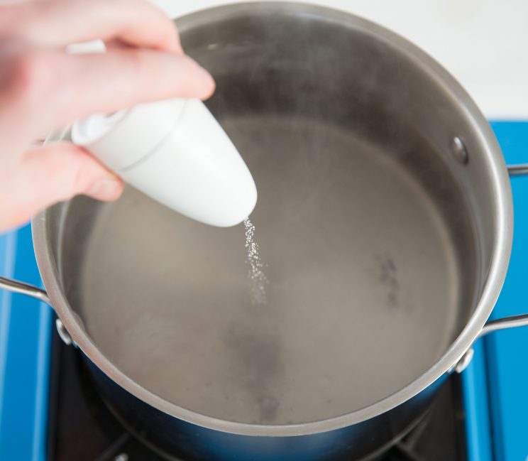 pouring salt into simmering pot of water