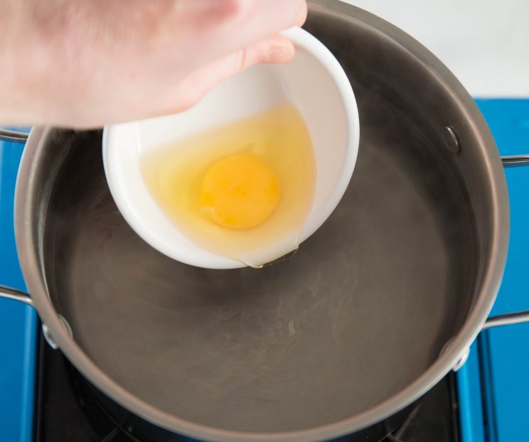 pouring egg into pot of simmer water from small white pot