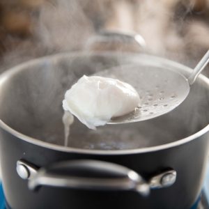 poached egg on a ladle above steaming pot of water