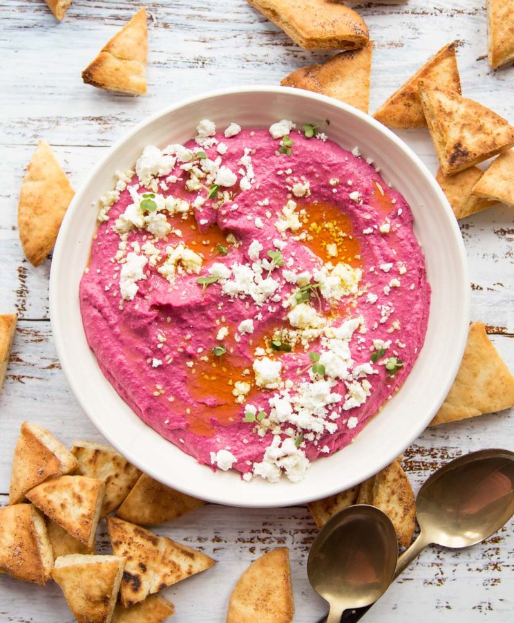 overhead shot of beet hummus garnished with feta surrounded by pita chips