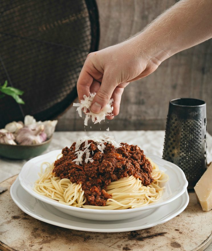 hand sprinkling parmesan over bolognese