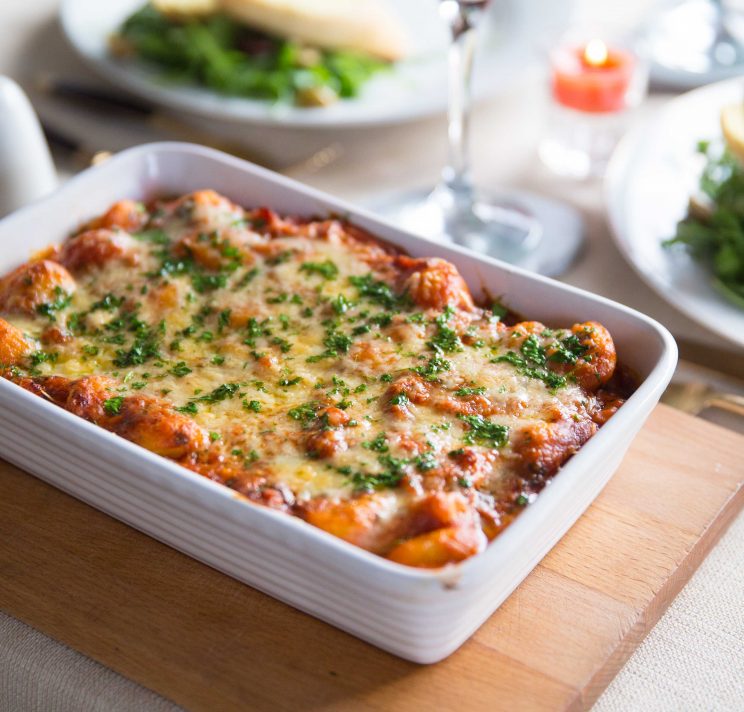 baked gnocchi served up with wine glass and candle blurred in background