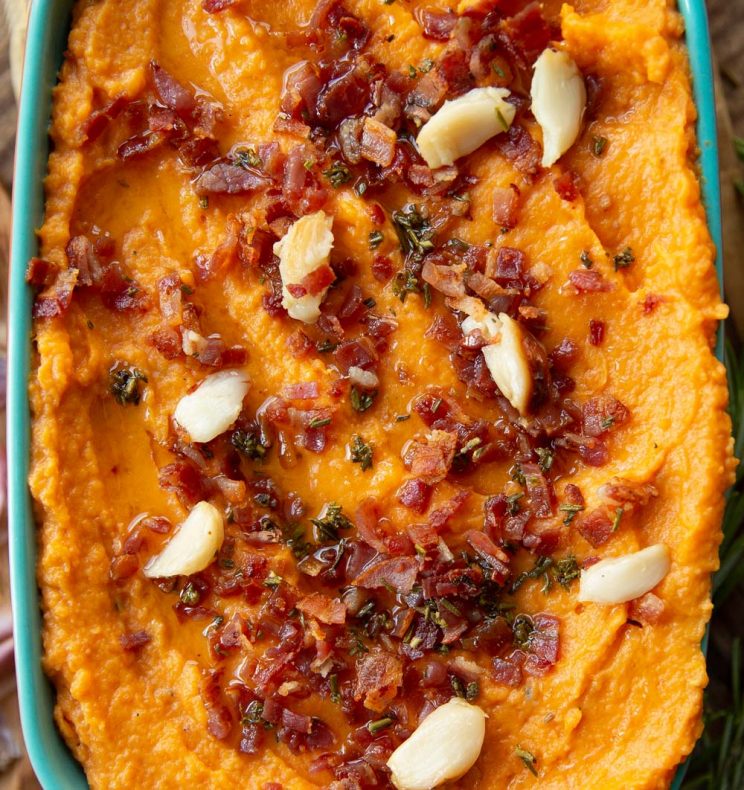 overhead shot of mash in baking dish garnished with bacon, rosemary and roasted garlic