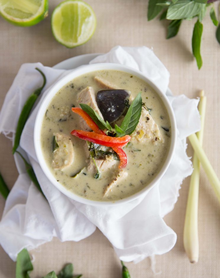 overhead shot of curry in white bowl on white cloth surrounded by garnish