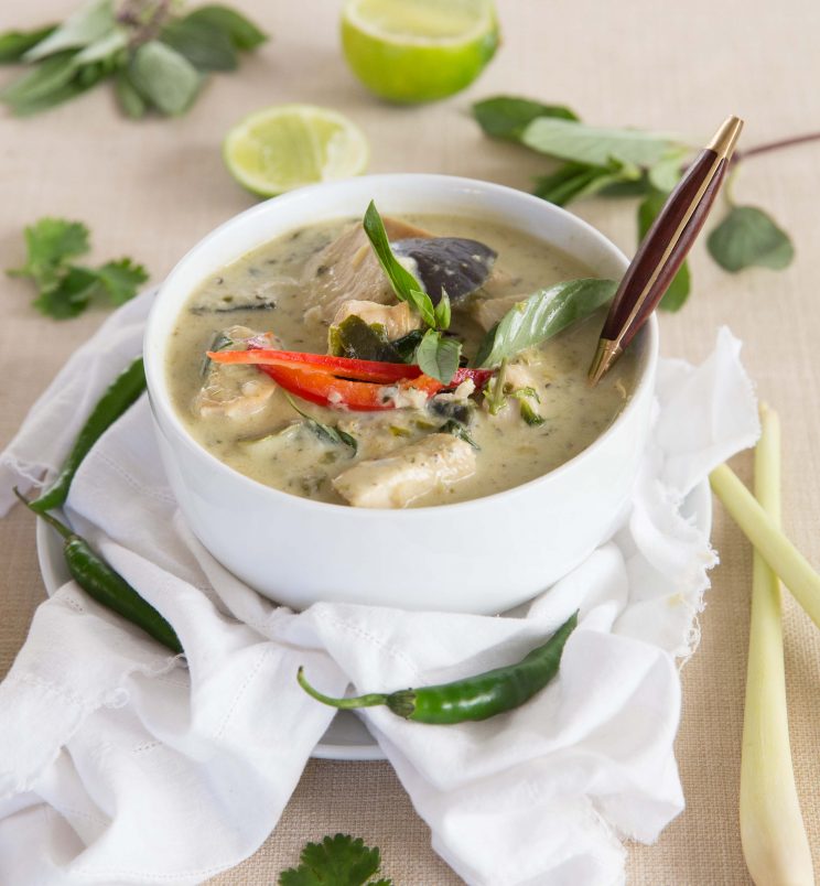 curry in a white bowl with gold spoon surrounded by garnish