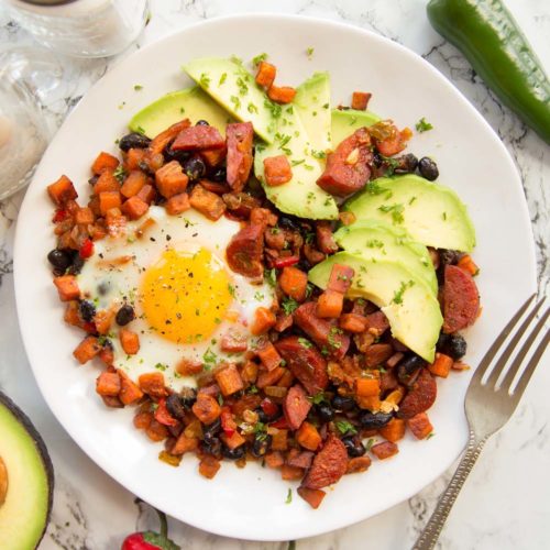 overhead shot of Sweet Potato Breakfast Hash on white plate served with avocado slices