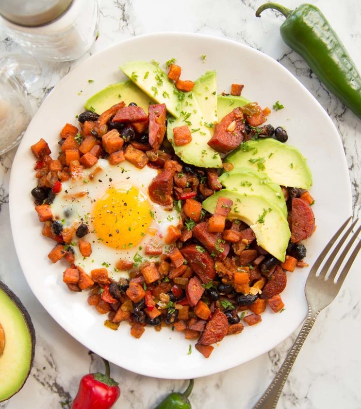 overhead shot of sweet potato hash and chorizo served on white plate with avocado slices