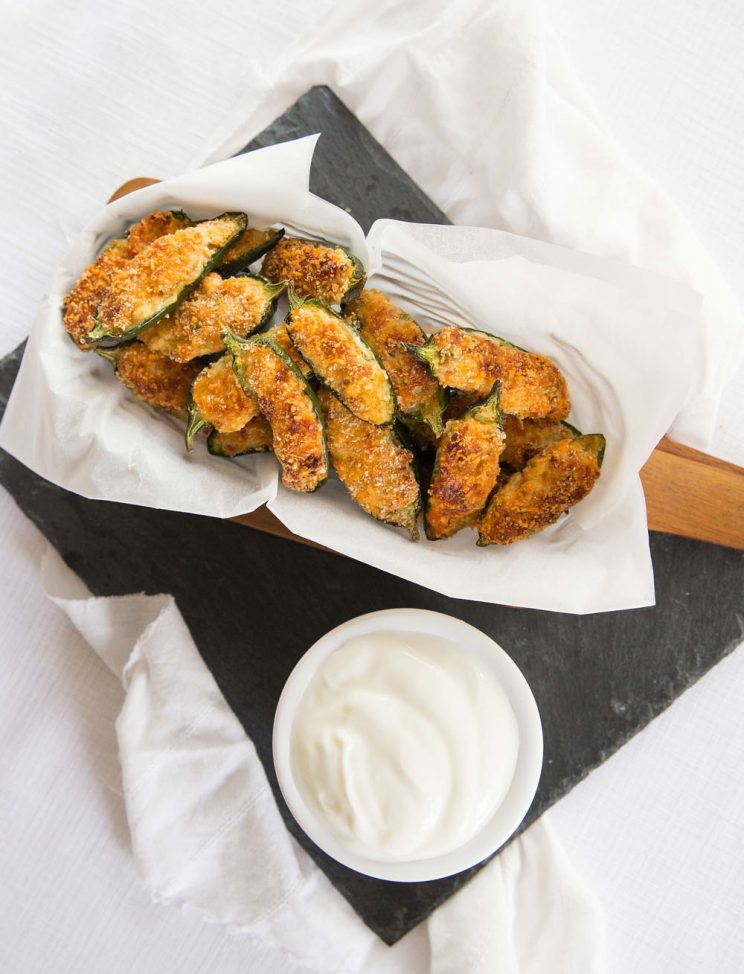 overhead shot of jalapeño poppers in basket with sour cream next to them 