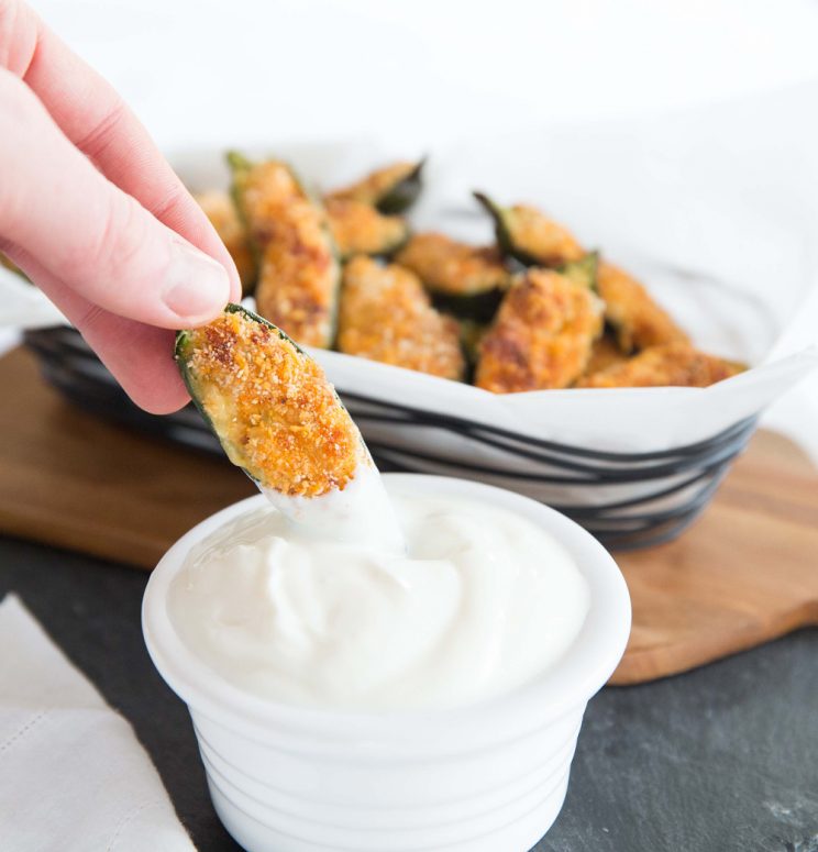 dipping jalapeño popper into pot of sour cream with basket blurred in background