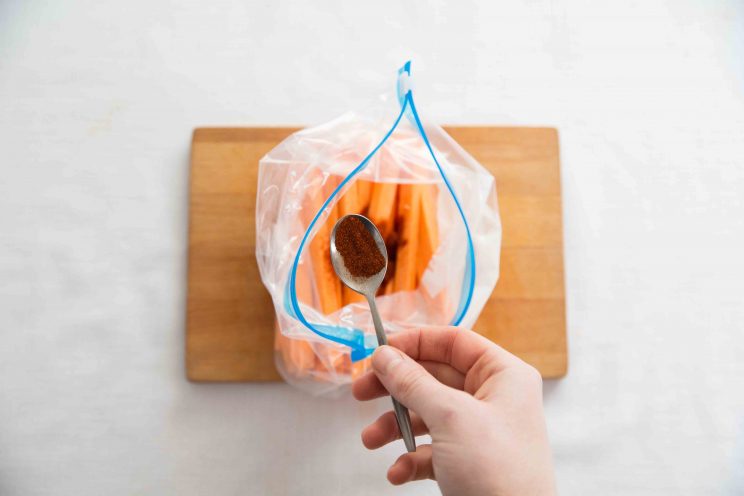 overhead shot of hand adding tbsp seasoning to zip lock bag of sweet potato fries