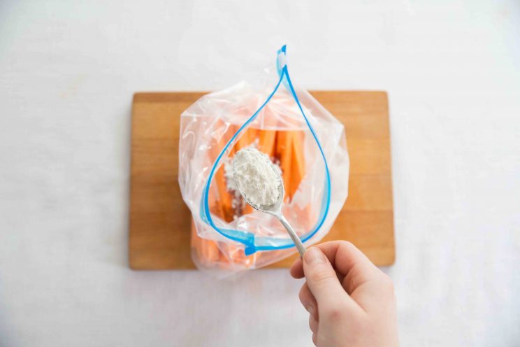 overhead shot of hand adding tbsp cornstarch to zip lock bag of sweet potato fries