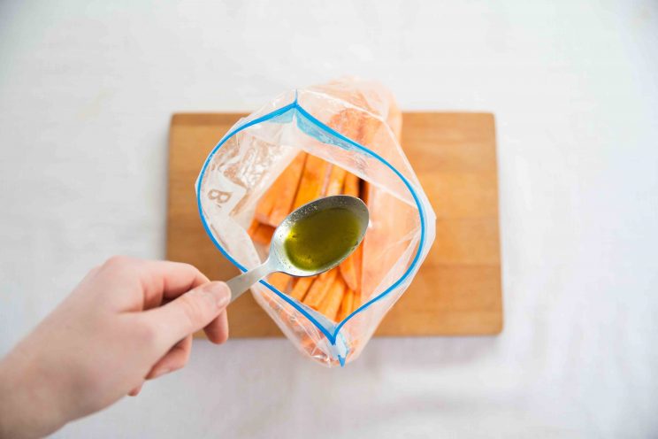 overhead shot of hand adding tbsp oil to zip lock bag of sweet potato fries