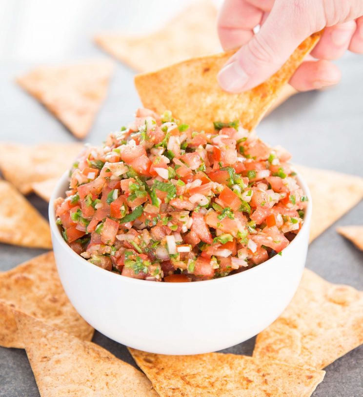 scooping tortilla chip into a bowl of salsa