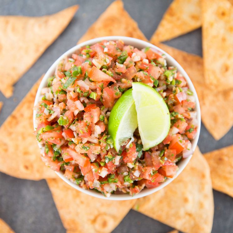 overhead shot of salsa in bowl with lime wedges and tortilla chips