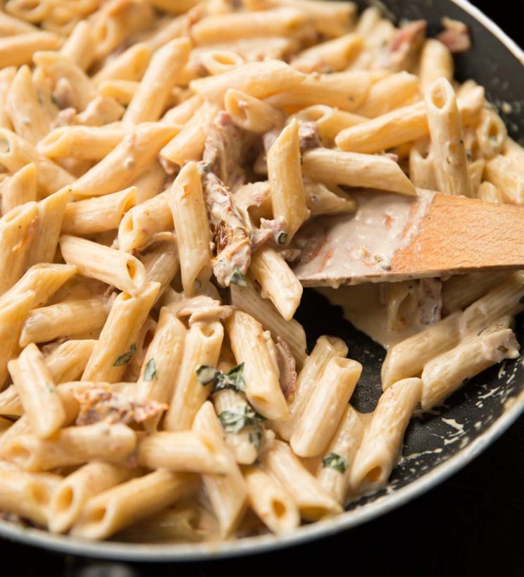 closeup shot of wooden spoon digging into pasta in skillet