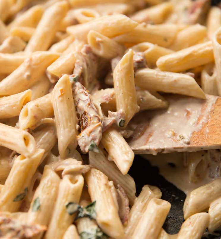 closeup shot of wooden spoon diving into skillet of creamy pasta