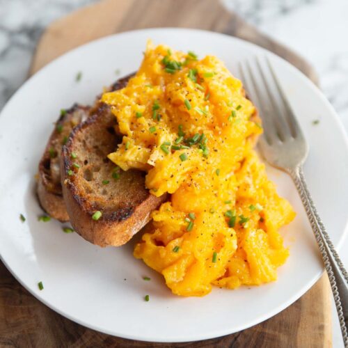 scrambled eggs served on two small slices of toast on white plate with silver fork