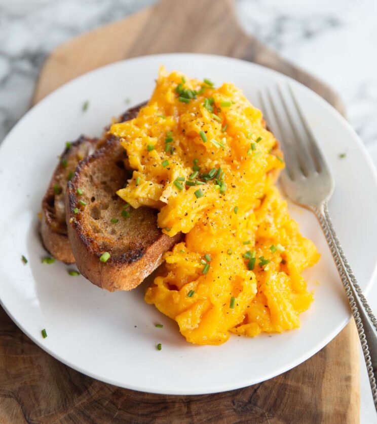 scrambled eggs served on two small slices of toast on white plate with silver fork