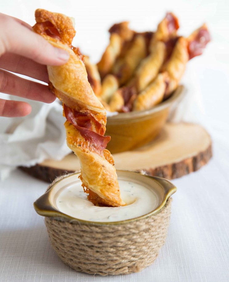 dunking cheese twist into small pot of sour cream dip with bowl of twists blurred in background