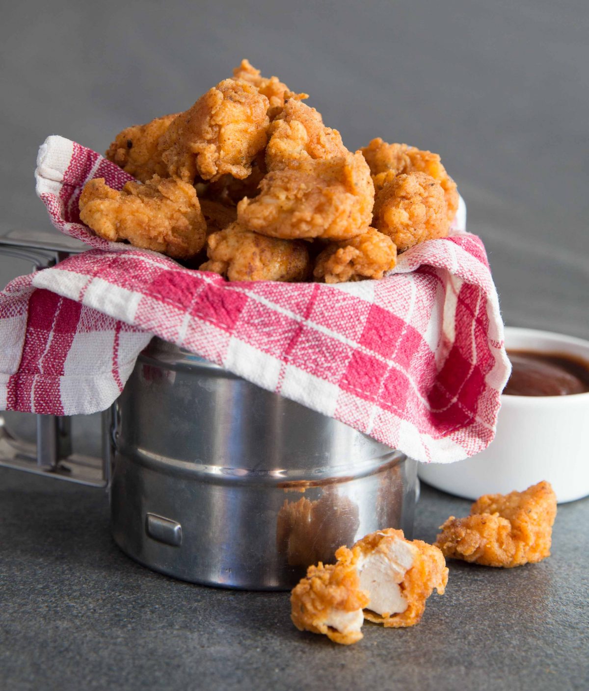 Popcorn Chicken in metal tub wrapped in tartan cloth with BBQ sauce in the background