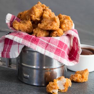 Popcorn-Hähnchen in Metallwanne, eingewickelt in Tartanstoff mit BBQ-Sauce im Hintergrund