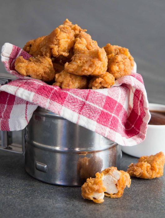 Popcorn Chicken in metal tub wrapped in tartan cloth with BBQ sauce in the background