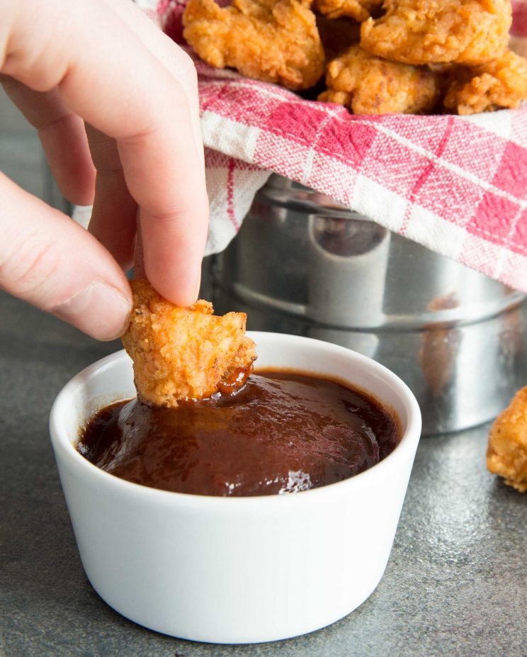 Hand dippt 1 Stück Popcorn-Hähnchen in einen kleinen Topf mit BBQ-Sauce