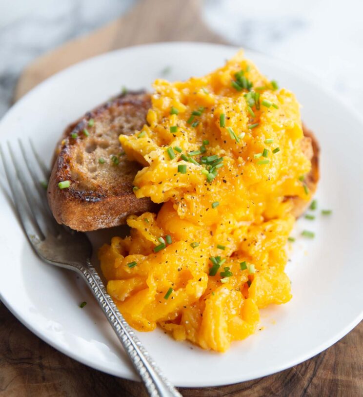 scrambled eggs served on toast with silver fork on white plate
