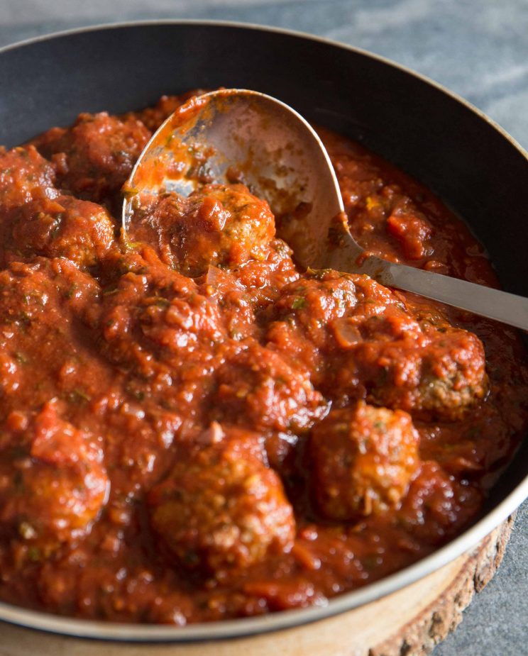Homemade meatballs in sauce in a frying pan scooping out with serving spoon