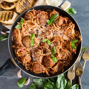 overhead head shot of spaghetti meatballs in pan surrounded by forks, fresh basil and garlic bread