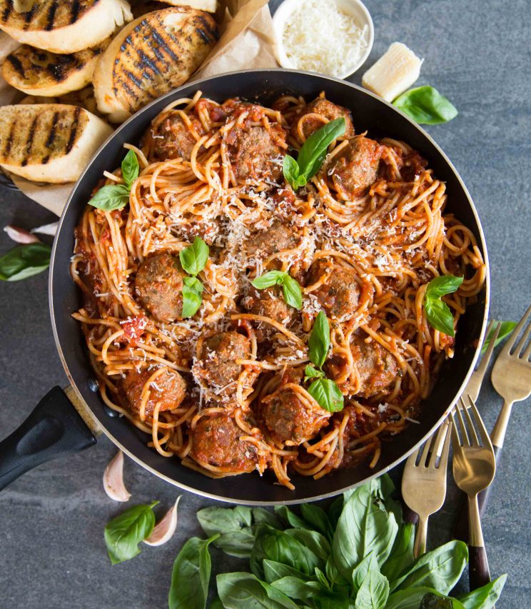 overhead shot of spaggheti meatballs in skillet surrounded by forks, fresh basil and garlic bread