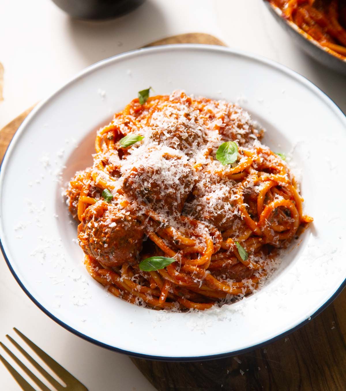 spaghetti meatballs served in small white dish with parmesan and basil