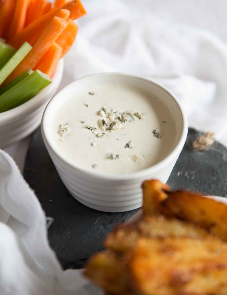 Homemade Blue Cheese Dip with sprinkled blue cheese on top and carrot/celery blurred in background