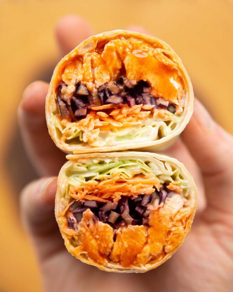 close up overhead shot of hand holding buffalo chicken wrap halves showing filling