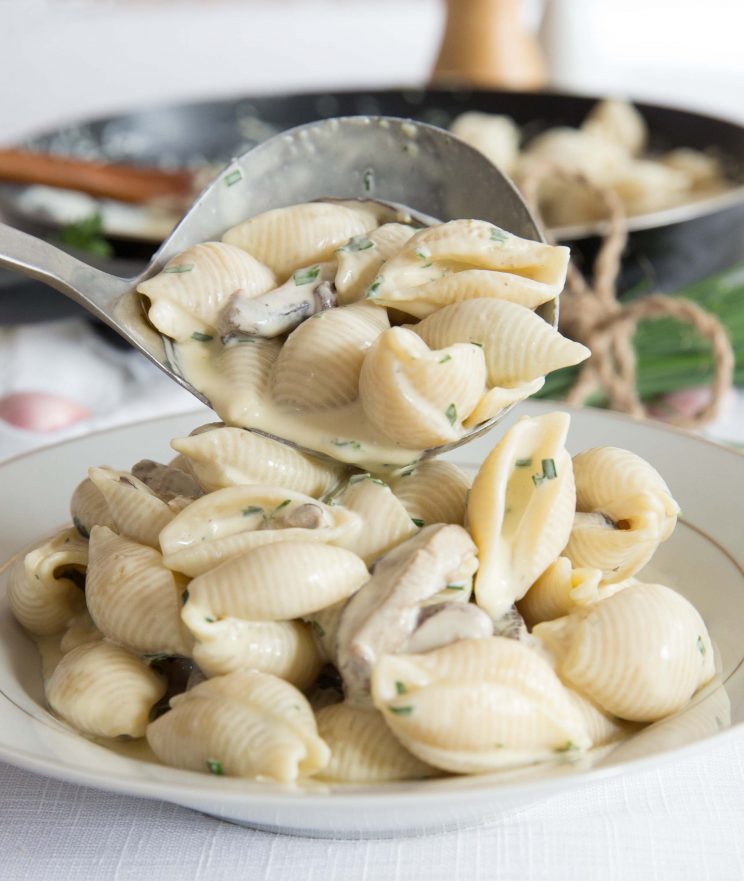 spooning pasta into bowl with skillet blurred in the background